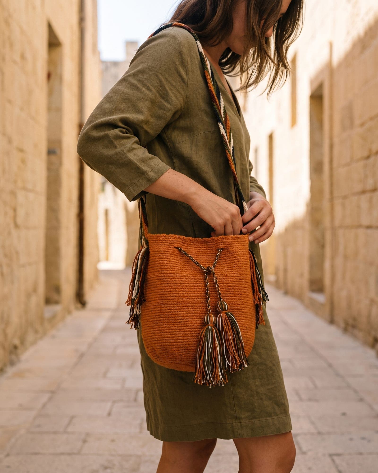 Die orangefarbene Mochila getragen — crossbody in einer Altstadtgasse, Hand am Zugband